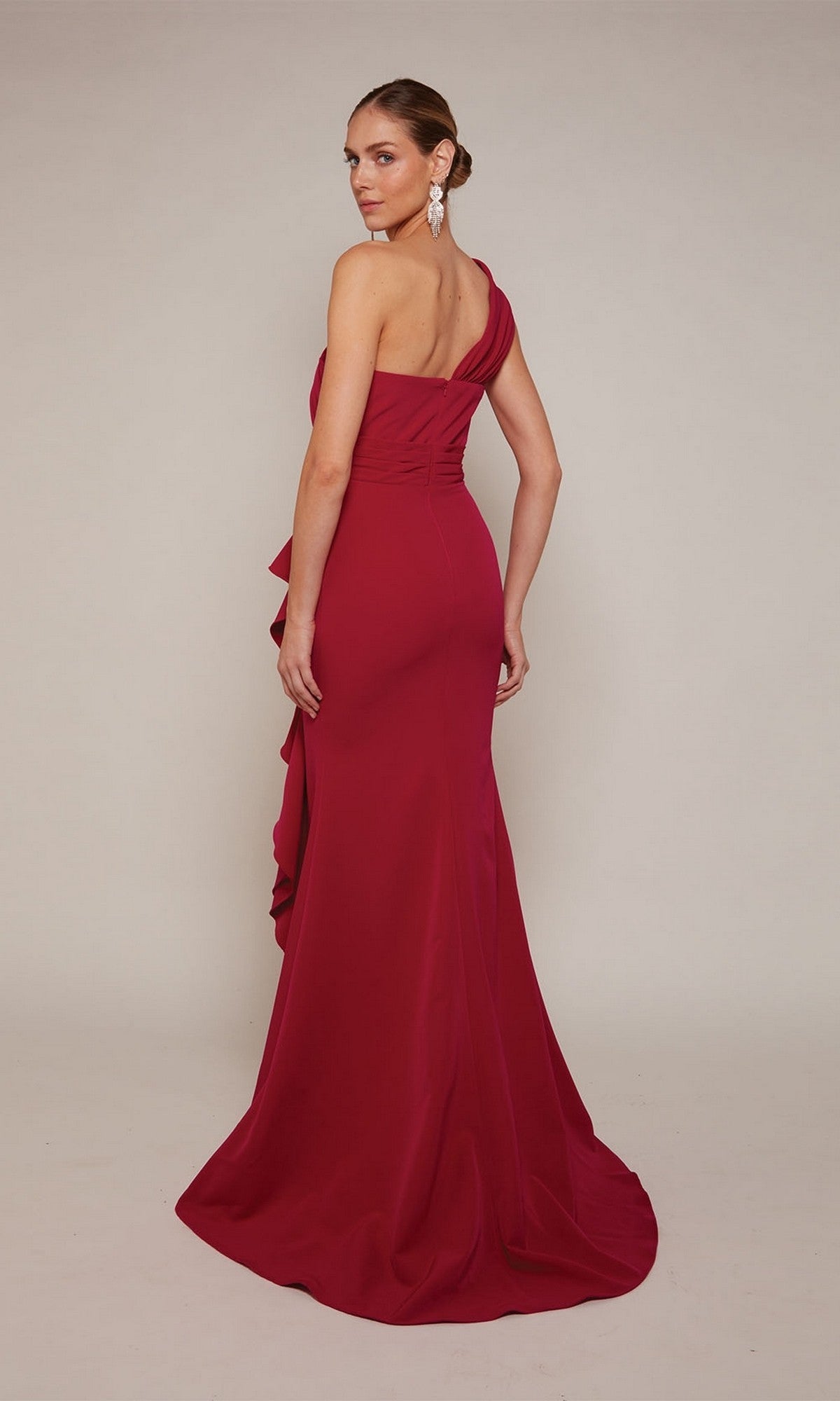 A woman faces away at a slight angle, showcasing the Alyce 27646 long formal dress with a floor-length, one-shoulder sheath silhouette, her hair in an updo accented by dangling earrings.